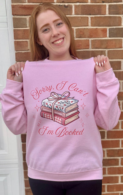 Person wearing a pink sweatshirt with a book-themed design in front of a brick wall.