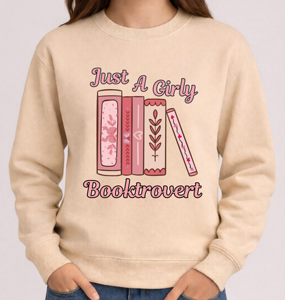 Beige sweatshirt with 'Just A Girly Bookdrovert' text and book illustrations on a plain background